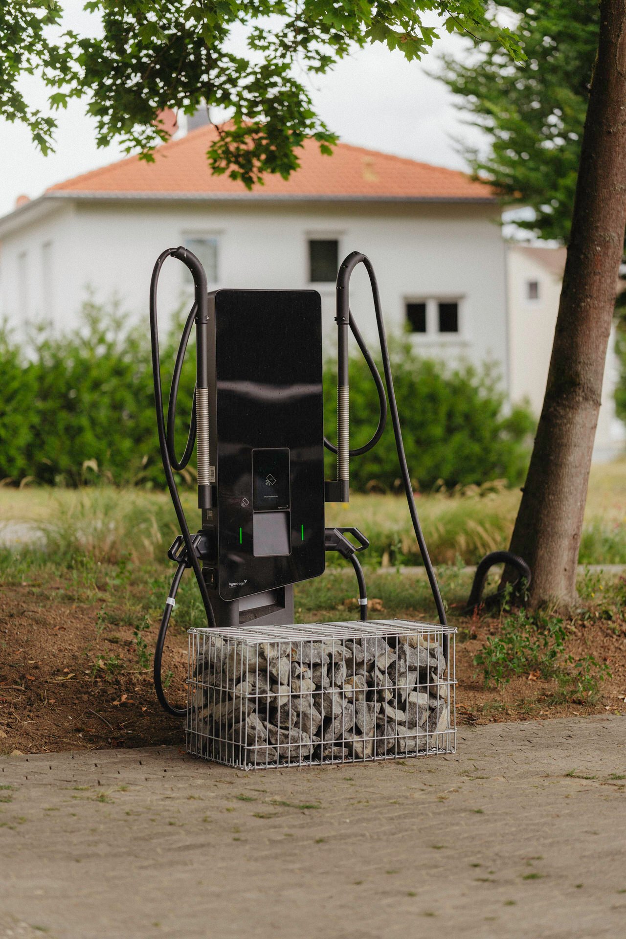 Schwarze Ladesäule für Elektroautos unter Baum.