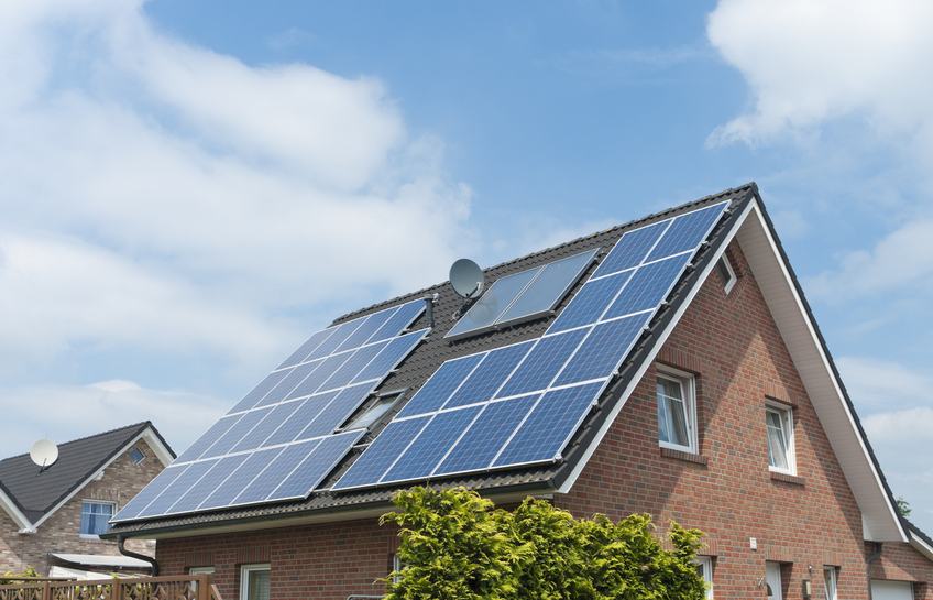 Wohnhaus mit Solarmodulen auf dem Ziegeldach unter blauem Himmel